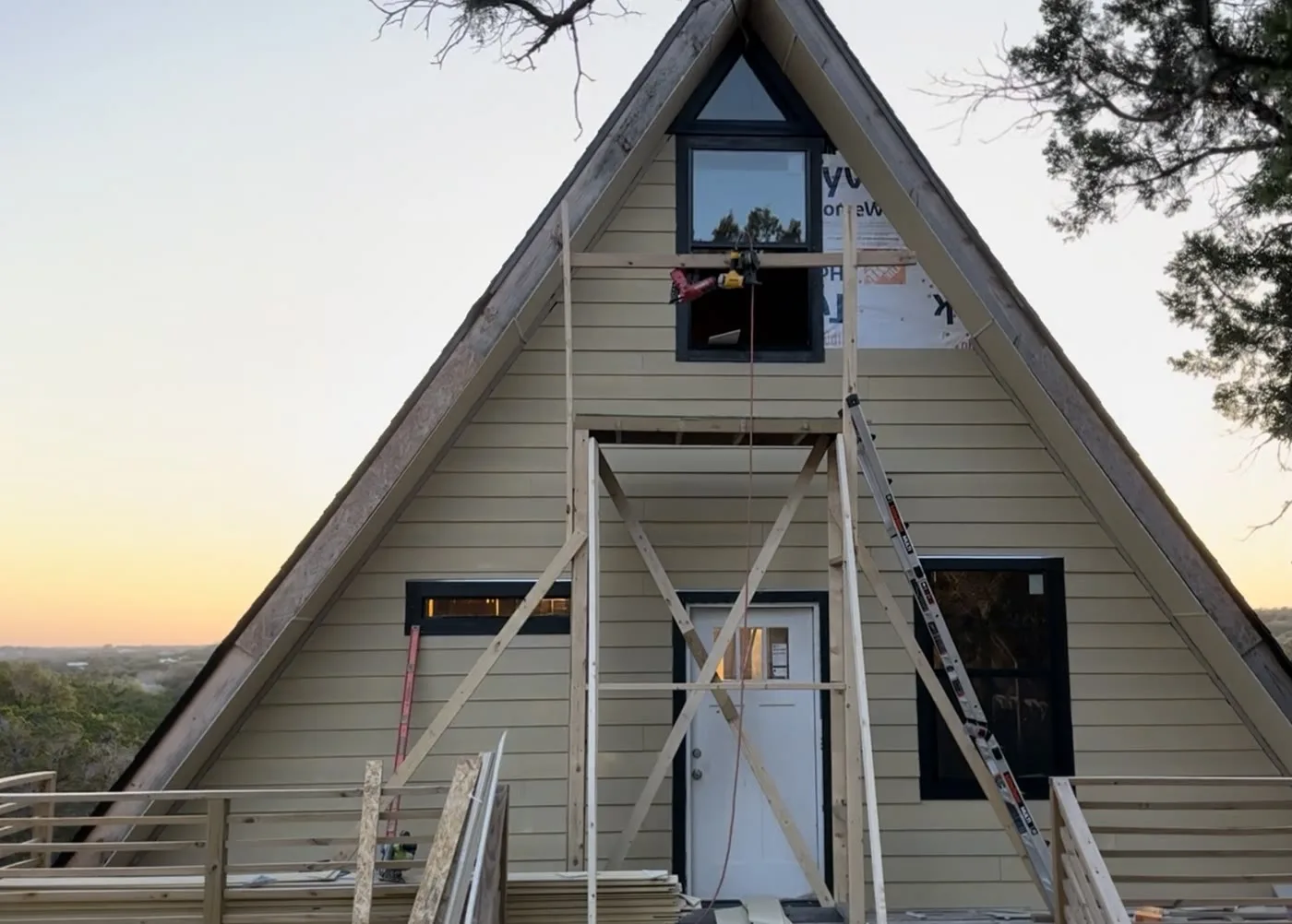 The completed A-frame at dusk, clad in pale siding with black window frames.